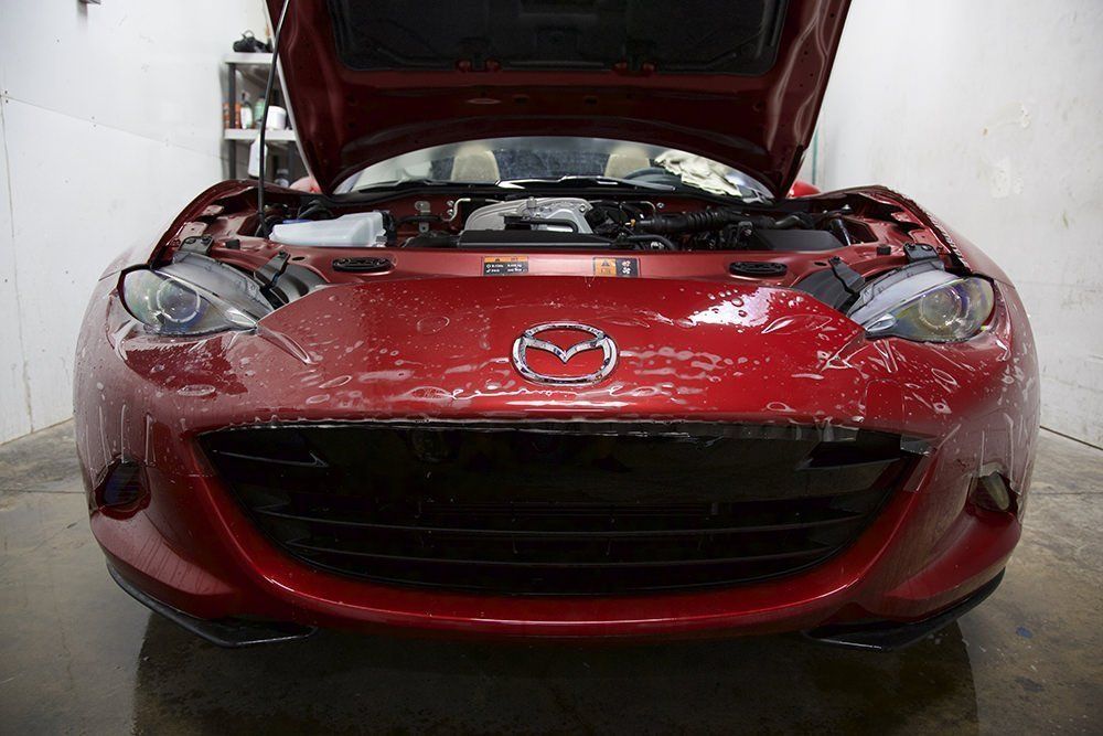 Red Mazda Miata with hood open, parked inside.