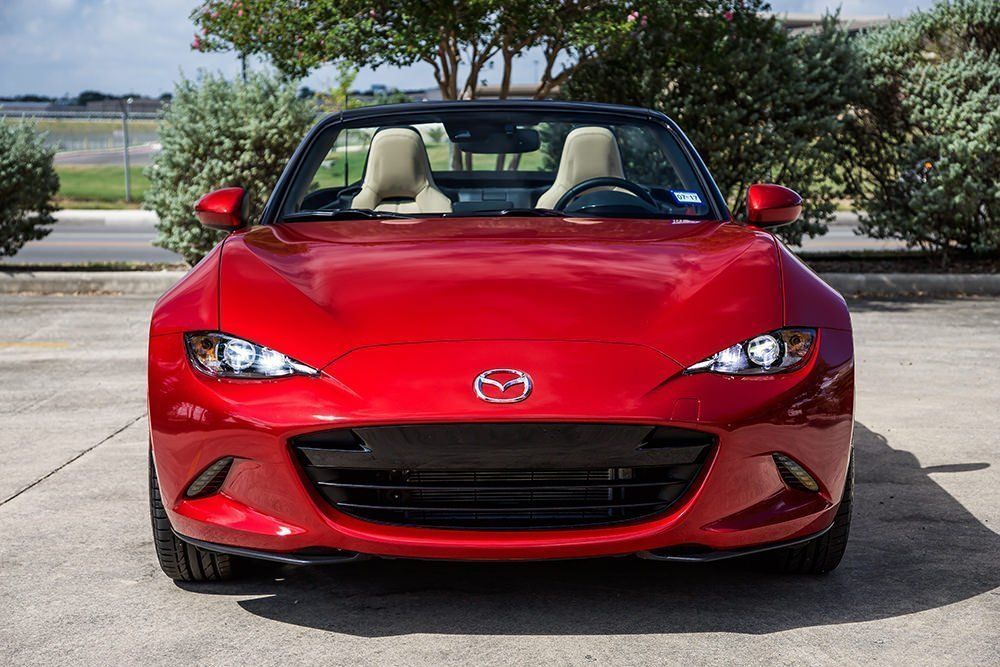 Red Mazda MX-5 Miata convertible parked outdoors, front view.