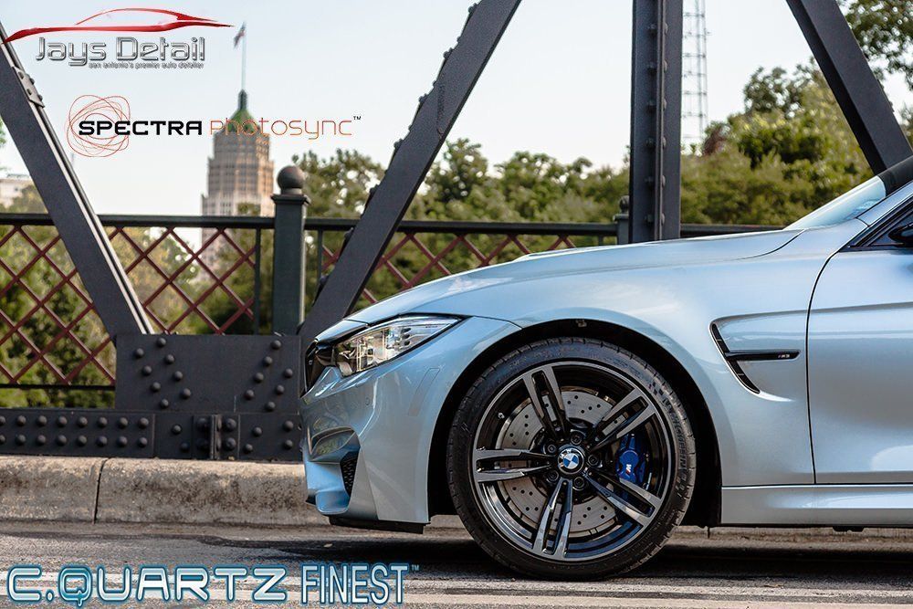 Silver BMW M4 sports car on a bridge with a city skyline in the background.