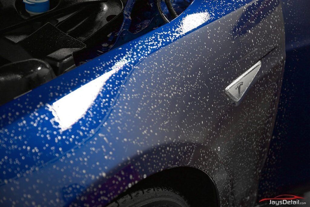 Blue Tesla car being sprayed with foamy soap in a car wash.