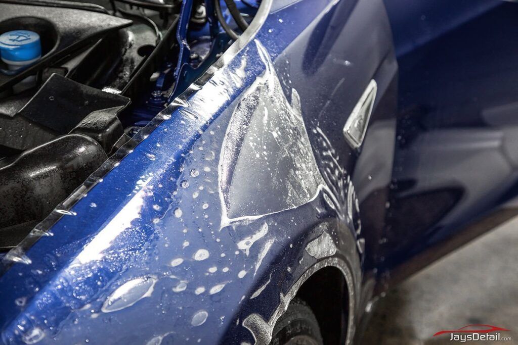 Blue car fender with partially removed clear paint protection film, wet with soapy water.