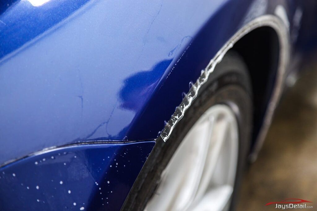 Blue car fender with paint damage near a tire.