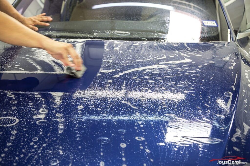 Person washing a blue car with soapy water using a sponge; indoor setting.