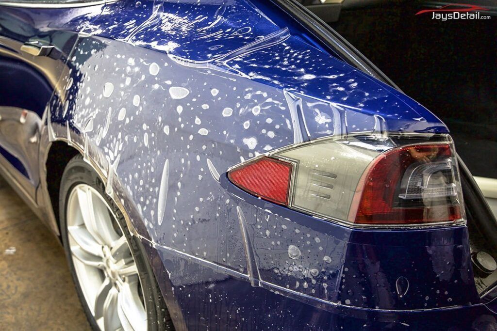 Blue Tesla being washed with soapy water; a detailing process.