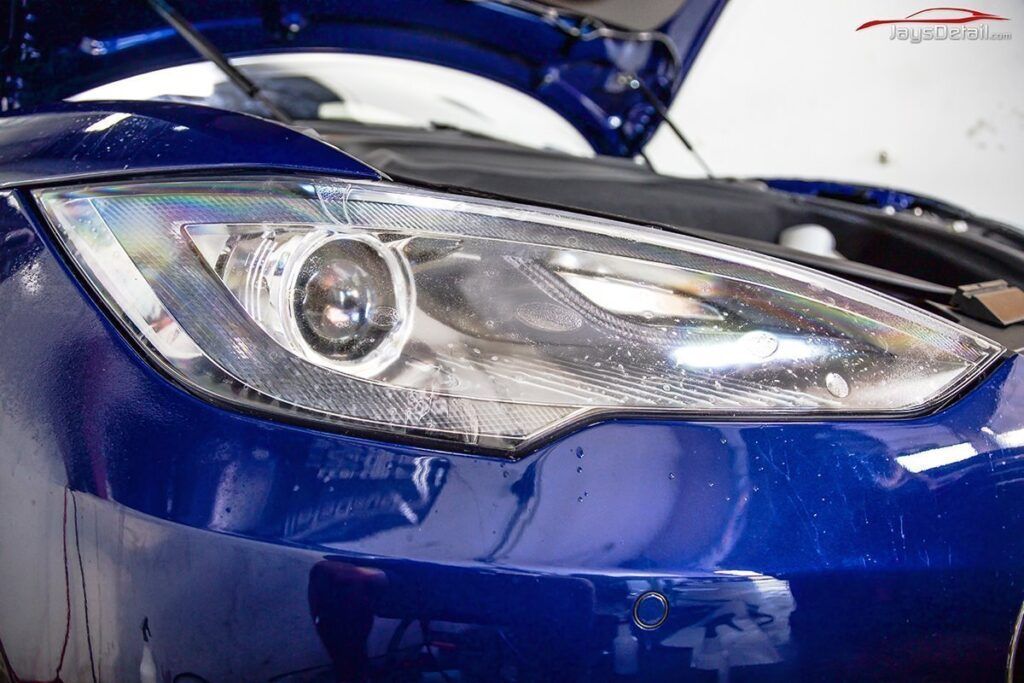 Blue Tesla car headlight, close-up with hood open, in a garage.