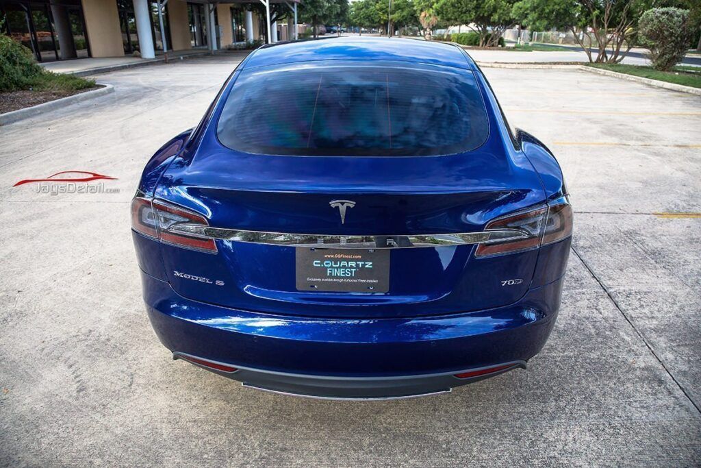 Blue Tesla Model S car parked on a paved surface with a retail building in the background.