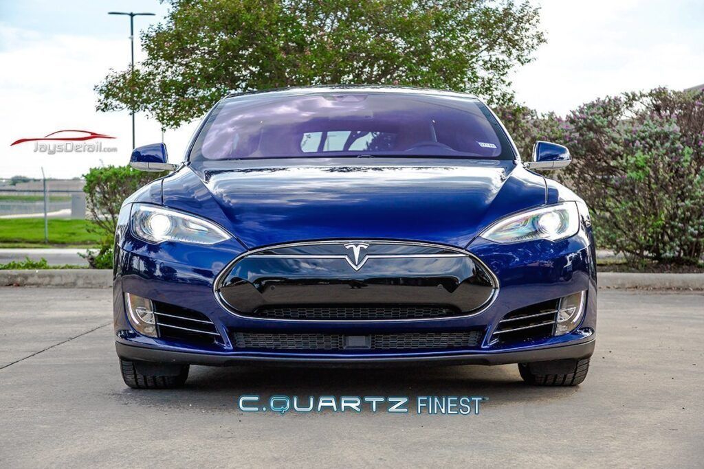 Blue Tesla car parked head-on; front view. Black grill, silver trim, and dark tinted windows; parked outdoors.