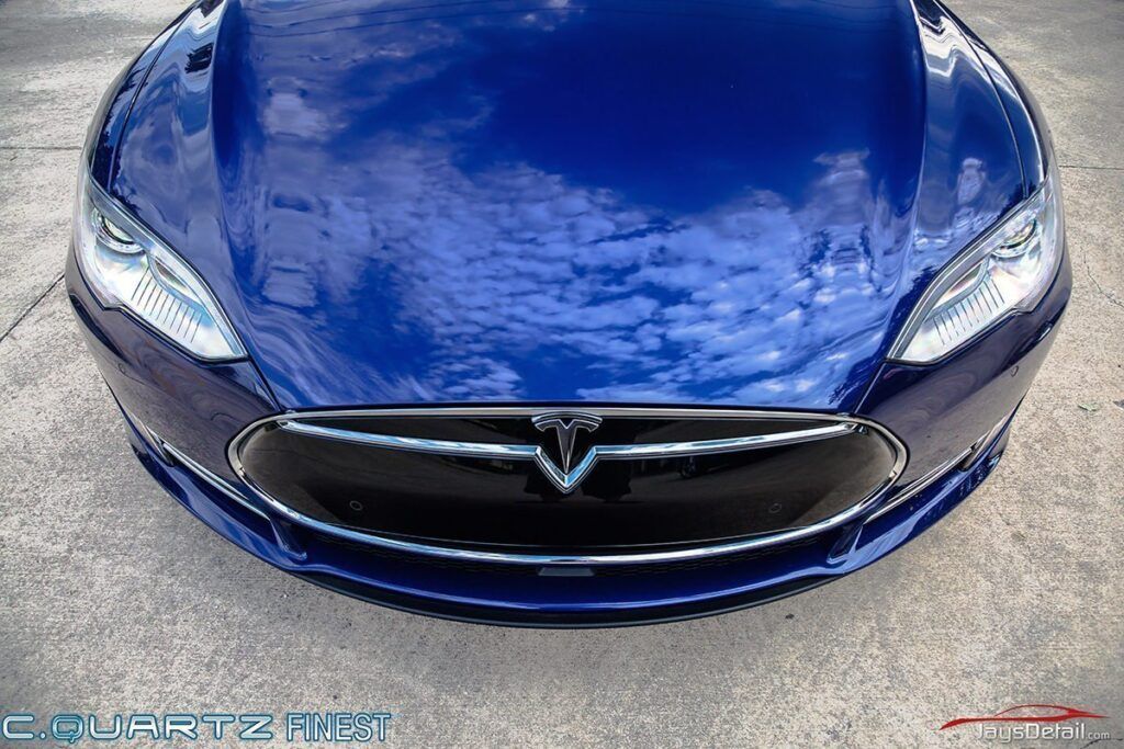 Blue Tesla car, front view, reflecting sky on hood.