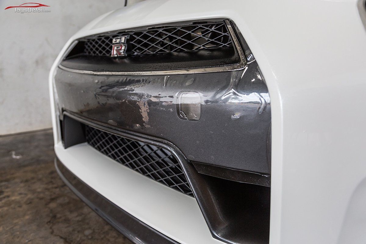 White Nissan GT-R front bumper with carbon fiber accents and damaged wrap.