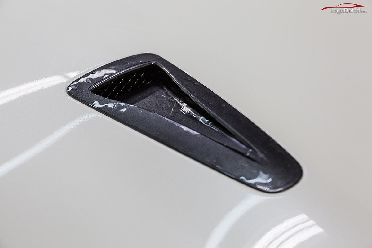 Black vehicle hood vent with chipped paint.