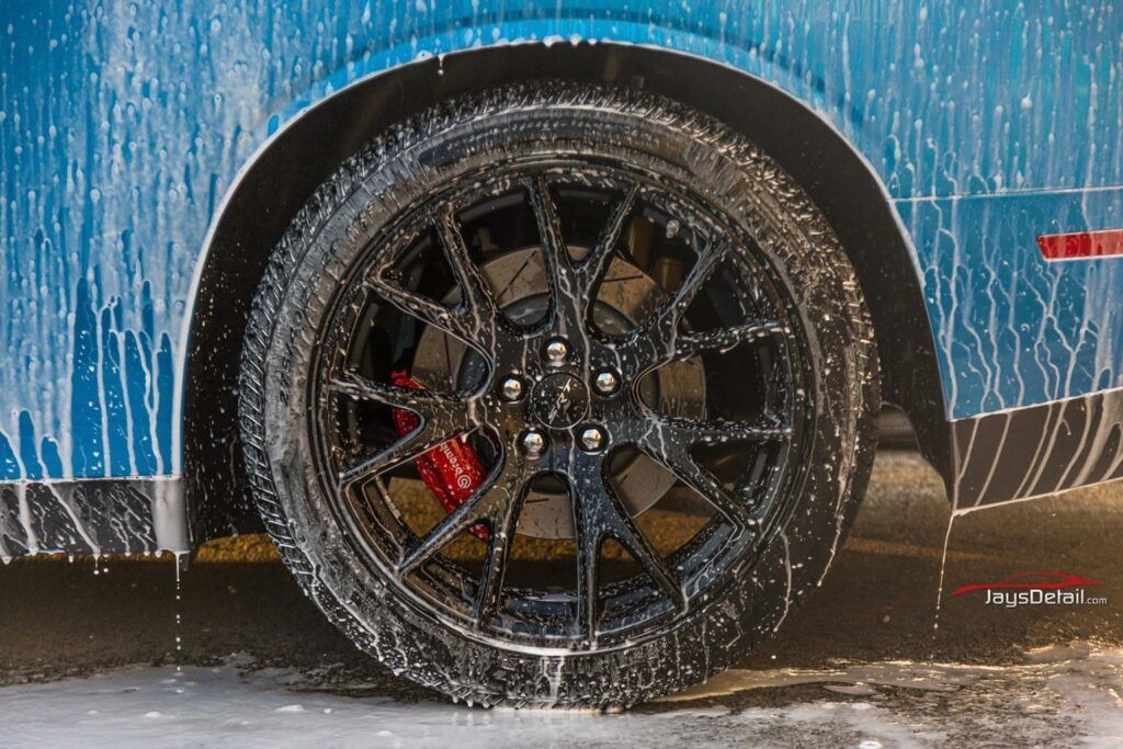 A close-up of a blue car's tire covered in white soap, with red brake calipers visible.