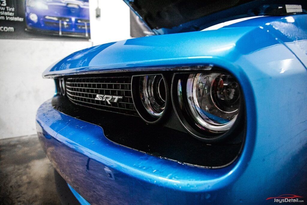 Close-up of a blue Dodge Challenger's front, including headlight and SRT grille, hood slightly open.