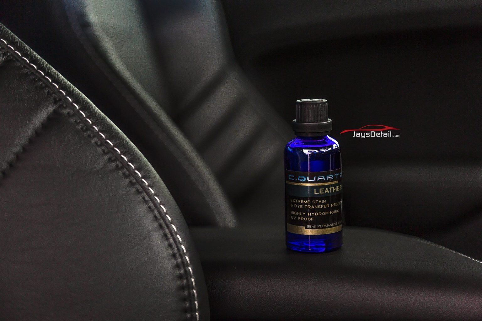 Blue bottle of car leather cleaner on a black leather car interior. White stitching visible.