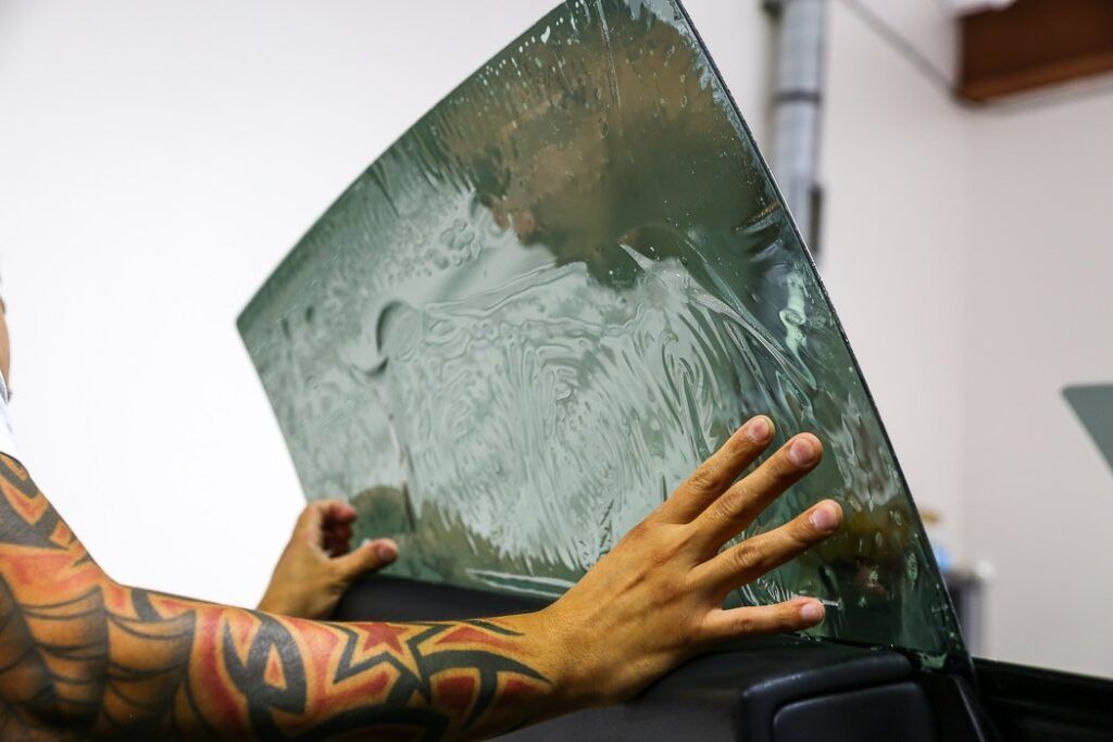 Person with tattoos applying tinted film to a car window.