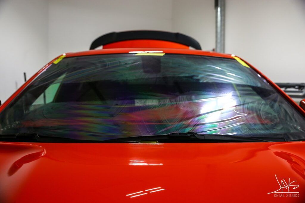 Red car with windshield film, showing rainbow-like colors in a garage.