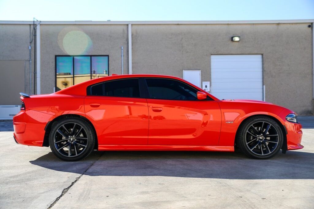 Bright orange Dodge Charger with black wheels parked outside a building.