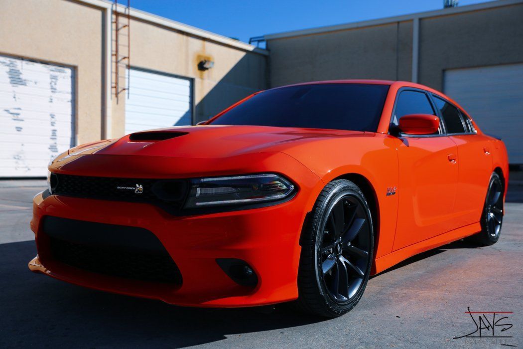 Orange Dodge Charger parked in front of a building with black wheels.