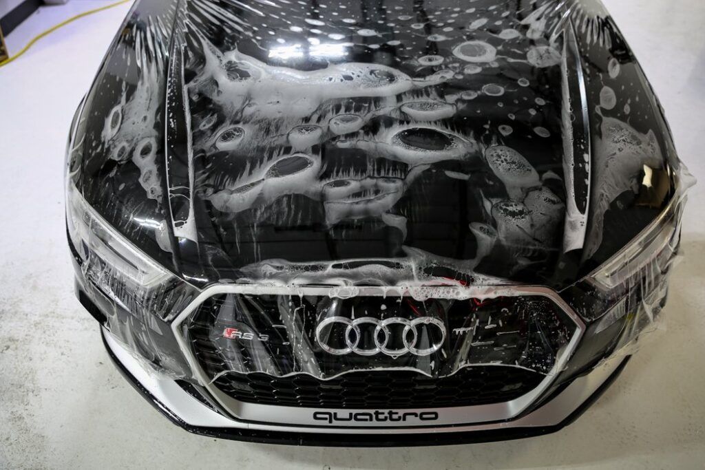 Black Audi car hood with protective film being applied.