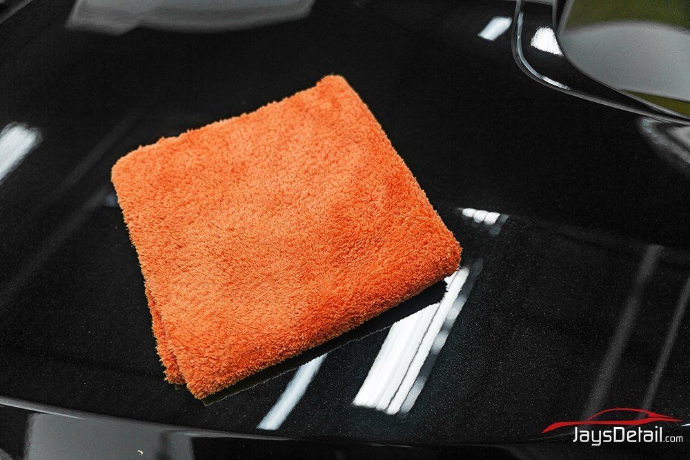 Orange microfiber cloth on a black car surface, likely detailing or cleaning.