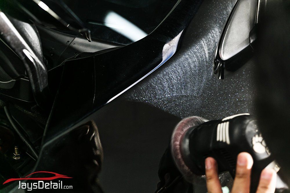 Person polishing a black car panel with a rotary buffer, removing scratches.