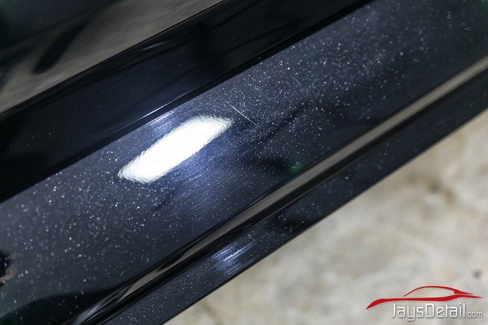 Black car door sill with scratches, white spot, and reflective flecks.