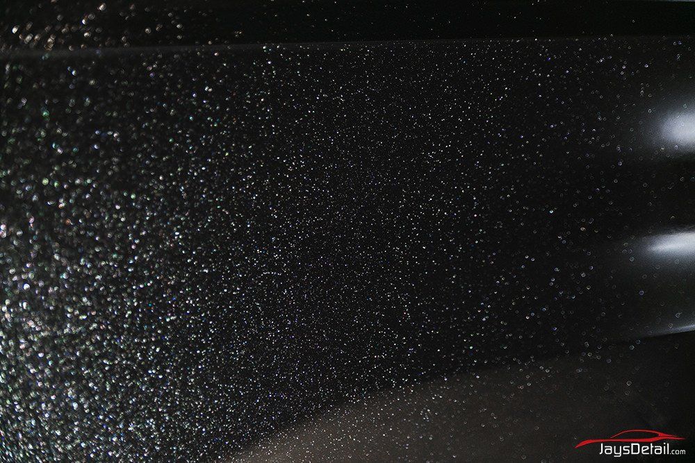 Close-up of black car paint speckled with glitter, reflecting light.