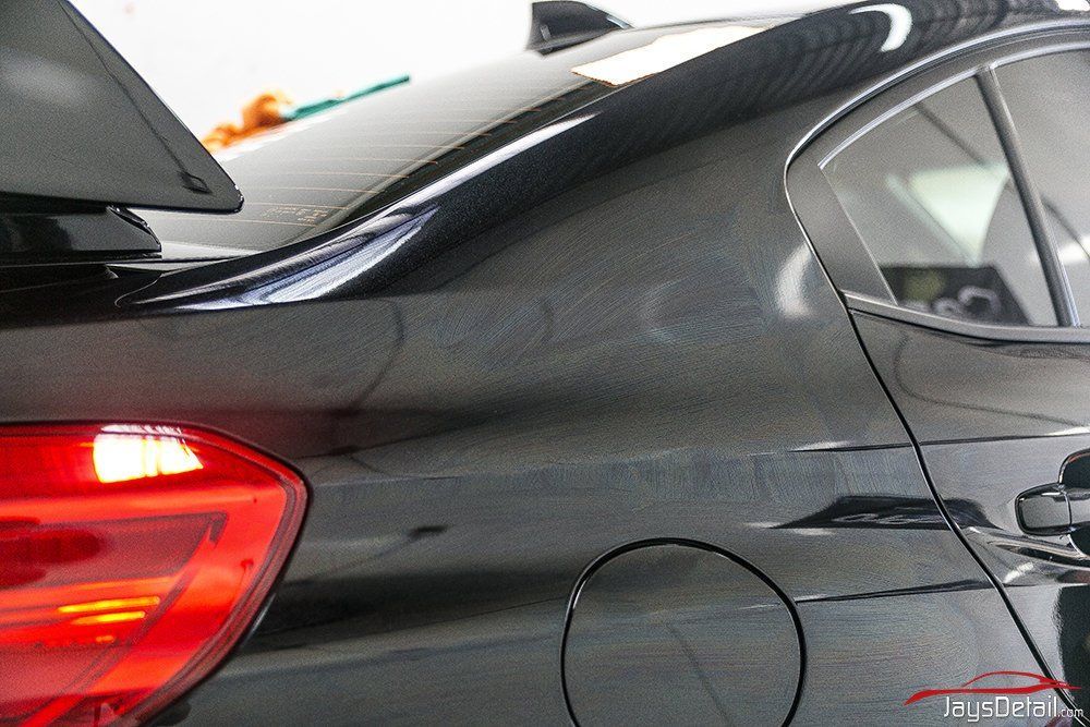 Black car rear with spoiler, tail light, and gas door, showcasing a textured wrap.