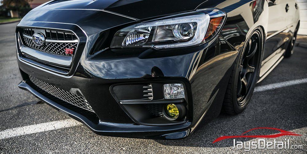 Black Subaru WRX STI with yellow fog lights parked on asphalt. Close-up front angle.