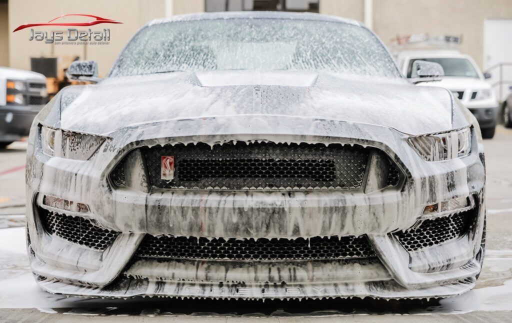 Ford Mustang covered in white foam at a car wash, viewed from the front.