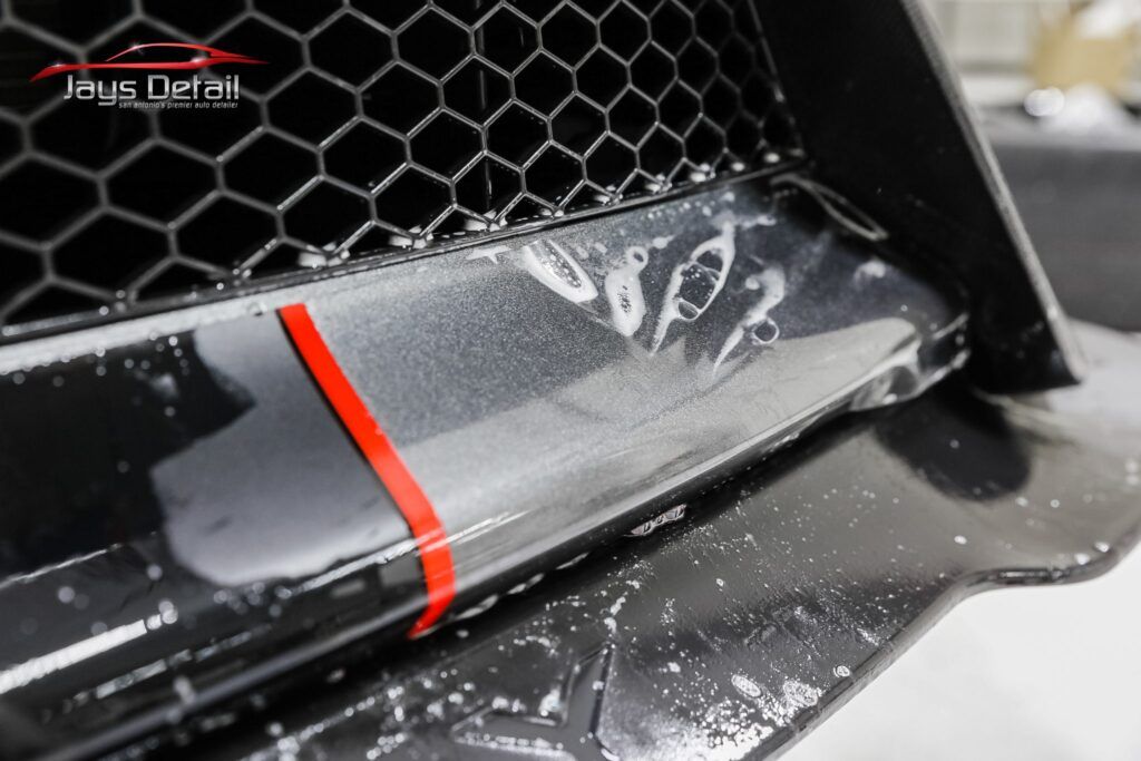 Black car bumper detail with red accent, covered in clear protective film.