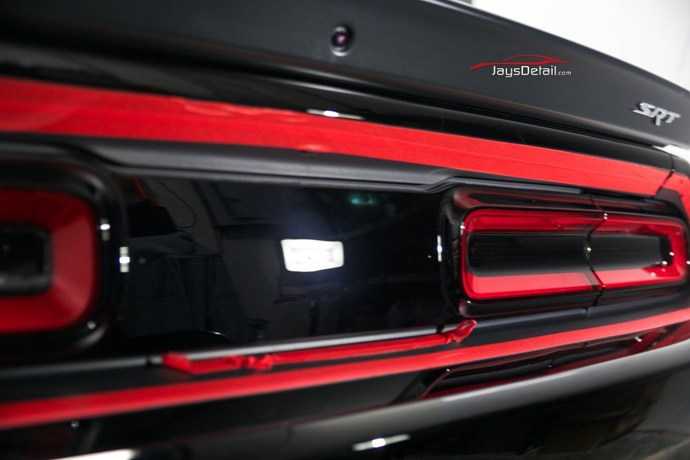 Close-up of a black Dodge Challenger SRT rear with red taillights, the car reflecting light.