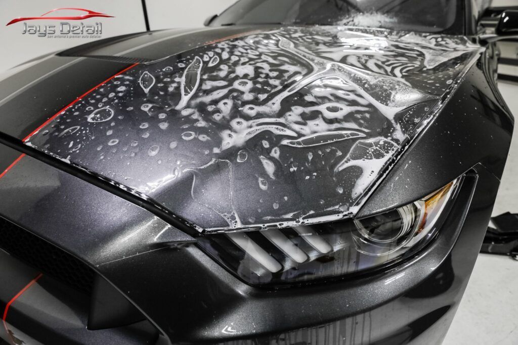Close-up of a gray Mustang's headlight being detailed, water droplets visible.