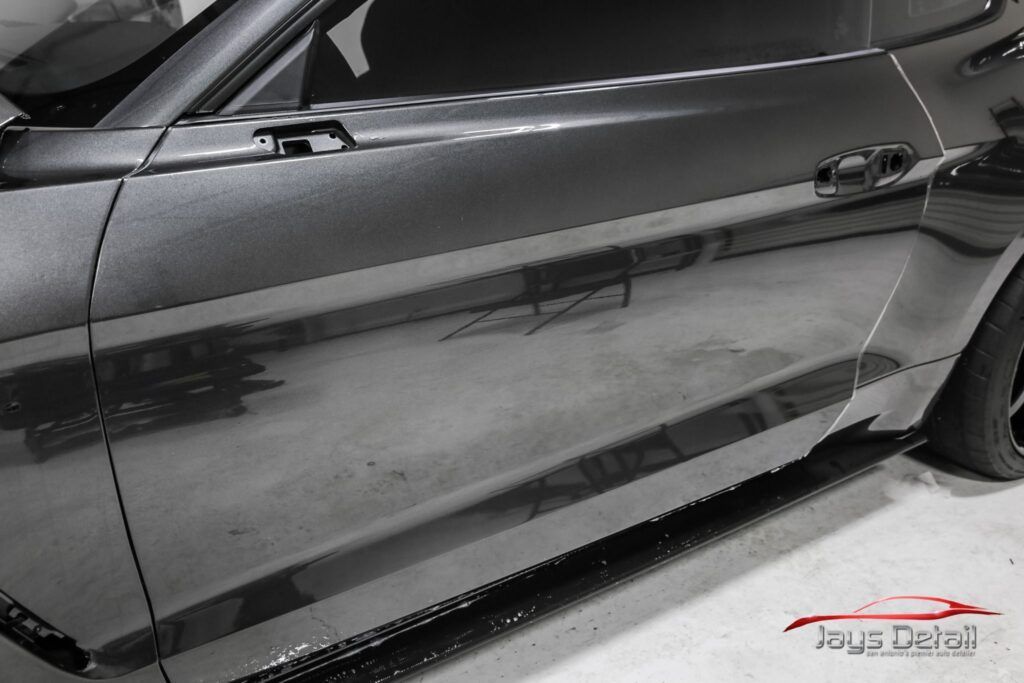 Shiny black car door reflecting surroundings, near a garage setting.