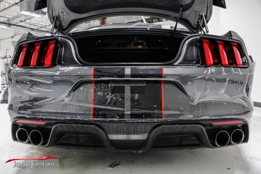 Rear view of a black Ford Mustang with trunk open, red taillights, and dual exhaust pipes.