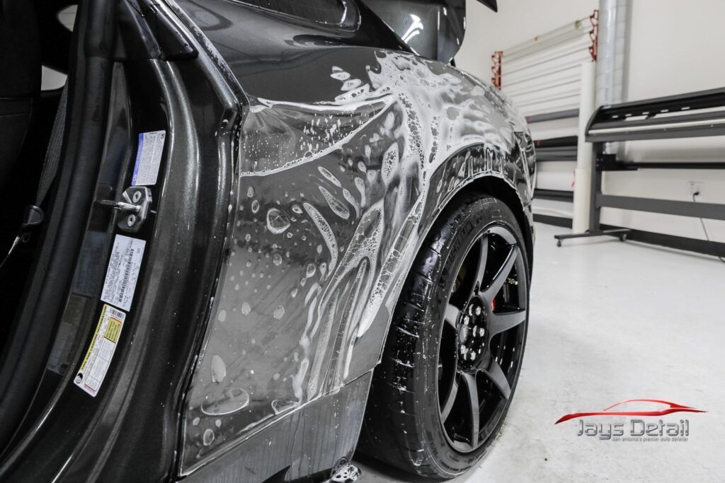 Black car being detailed with soap and water; in a garage.