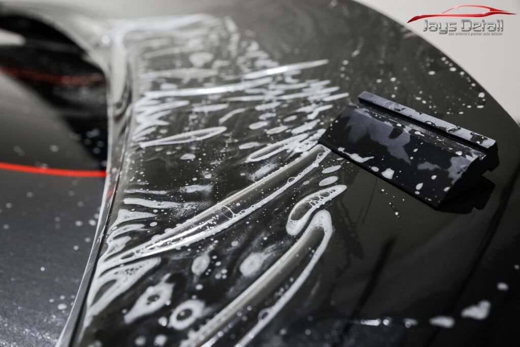 Applying protective film to a car hood with a squeegee; shiny black paint, close-up.