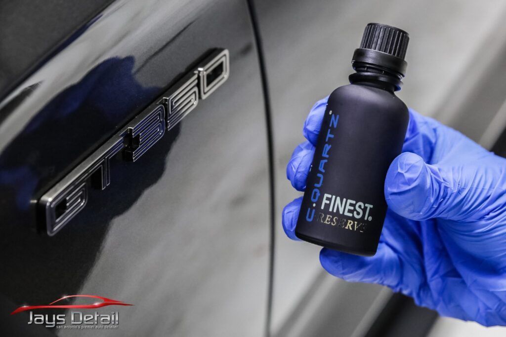 Person in blue gloves holds bottle of car ceramic coating next to 