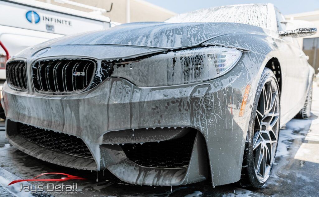 A gray BMW M4 being washed with foamy soap at a detailing shop.