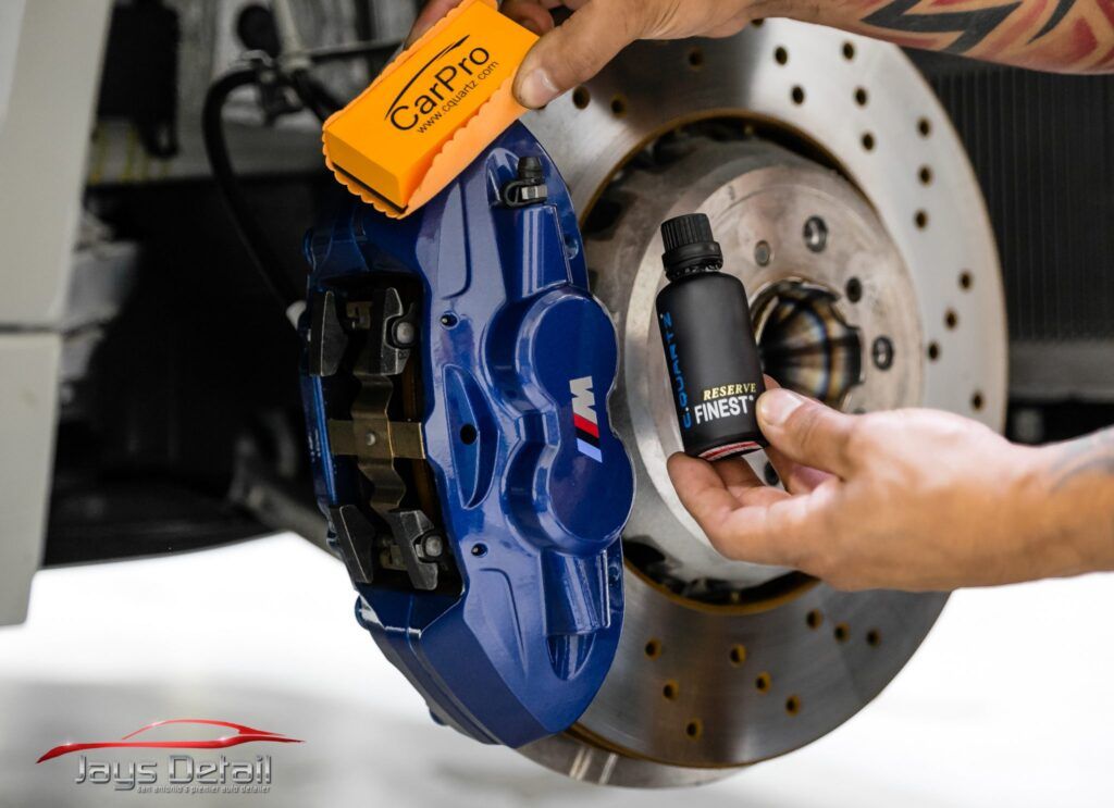 Person applying ceramic coating to a blue car brake caliper; product visible.