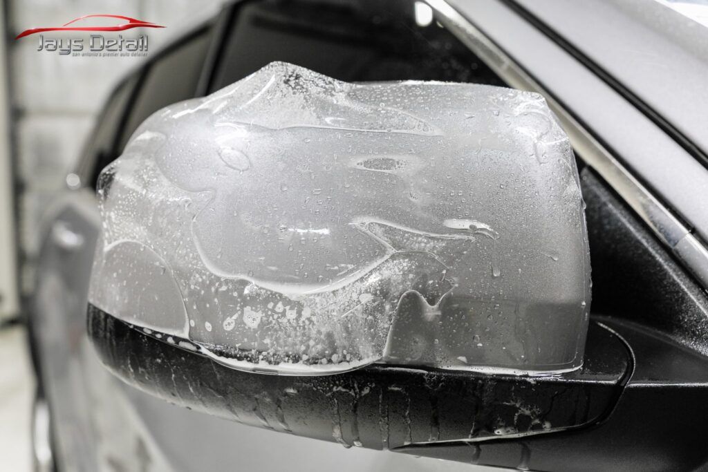 Car side mirror covered in wet, clear protective film.