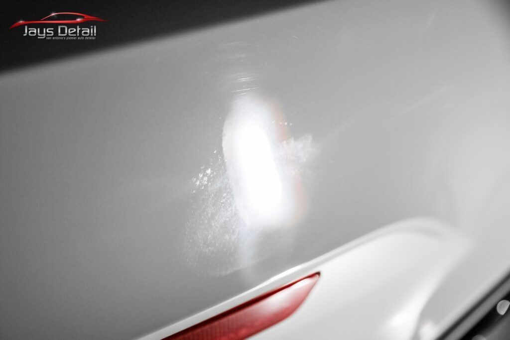 Close-up of a white car surface with swirl marks highlighted by a light.