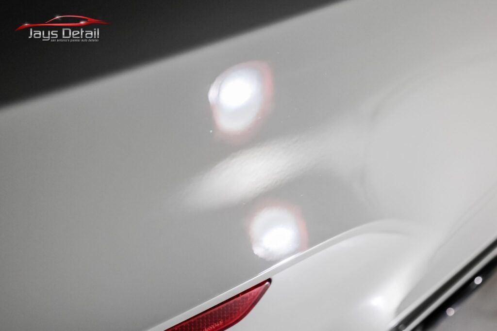 White car hood with shiny, reflective surface; red light detail.