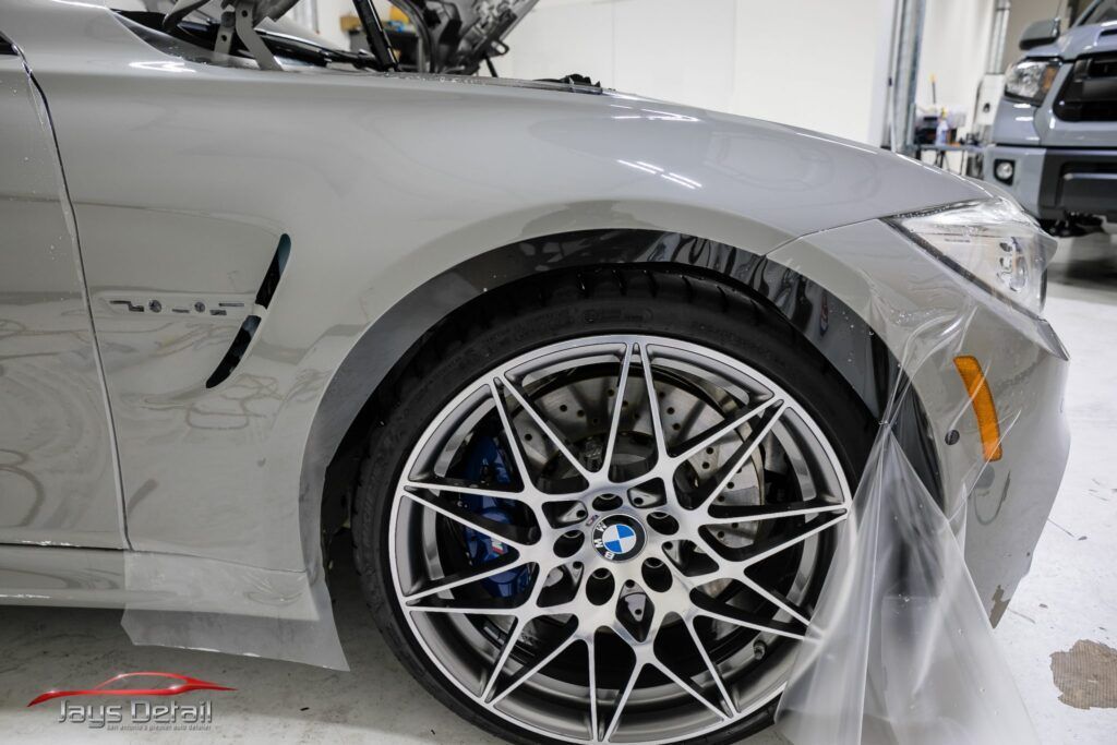 Silver BMW car wheel with blue brake calipers, being protected by clear film.