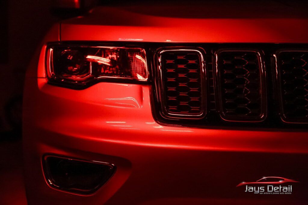 Red Jeep front end with headlight, grill, and bumper illuminated.