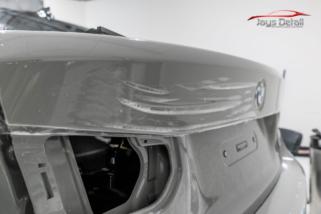 Rear view of a gray BMW car with a damaged trunk being repaired in a shop.