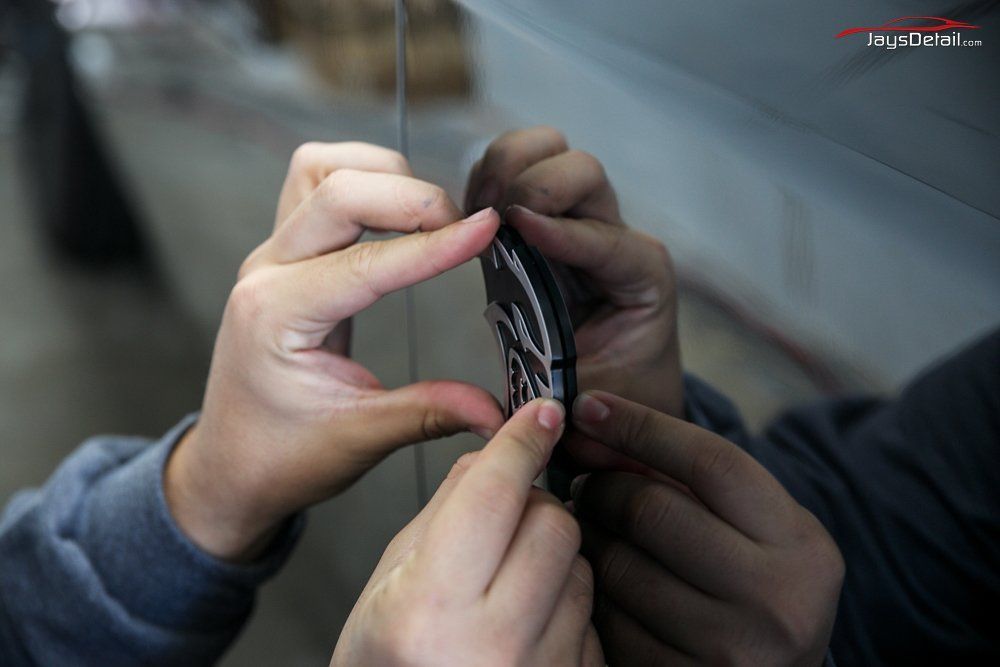 Two hands placing a black and white decorative emblem on a car's surface.