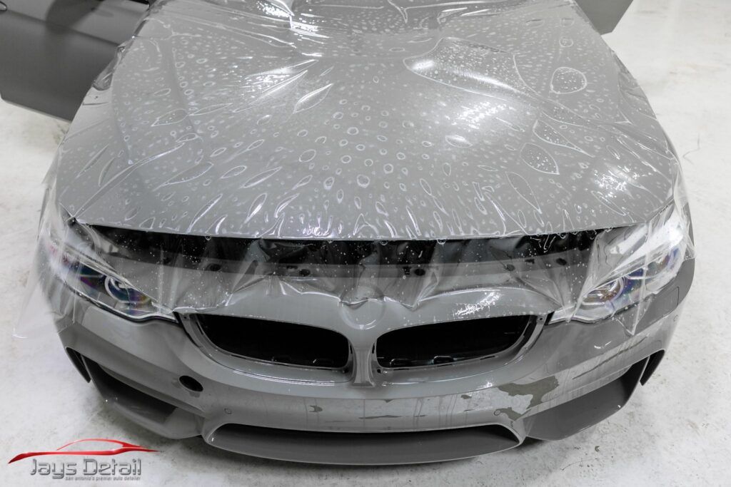 A gray BMW car front covered in protective clear film in a shop.