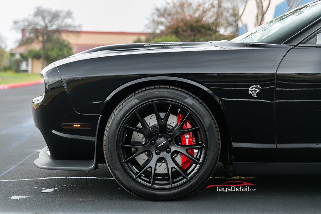 Black Dodge Challenger, front view, showing red brake calipers and black wheels.