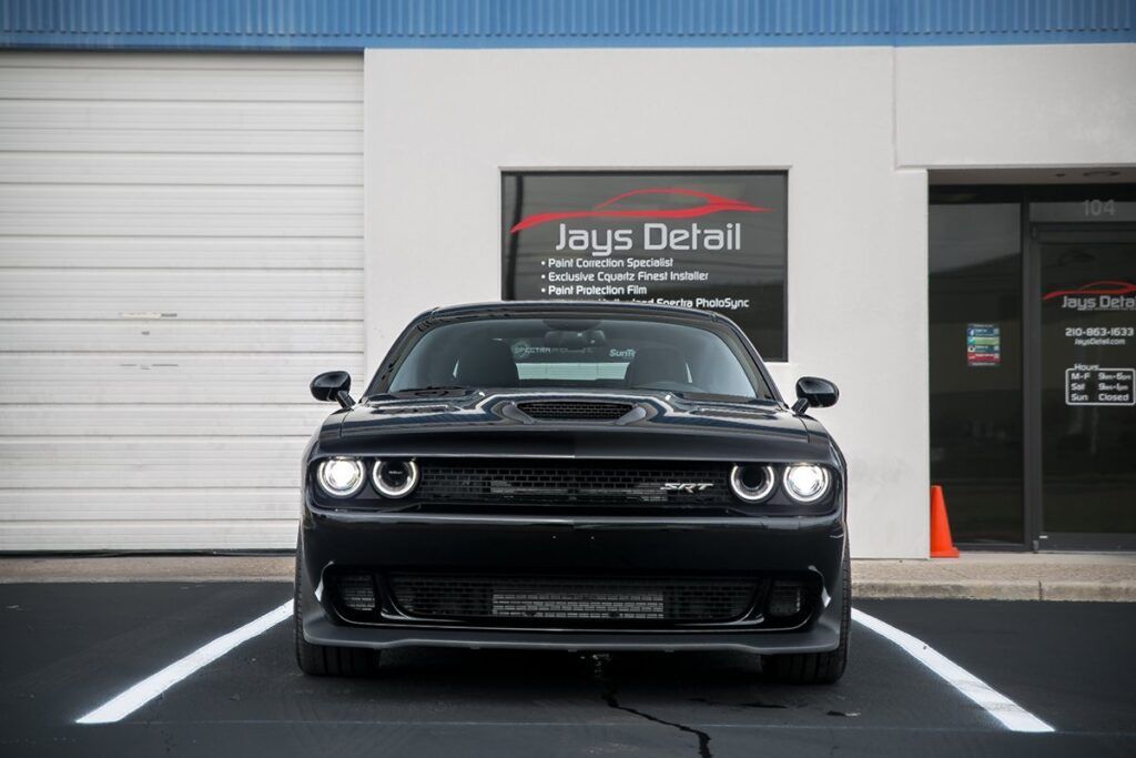 Black Dodge Challenger parked in front of Jay's Detail, a business with a white garage door.