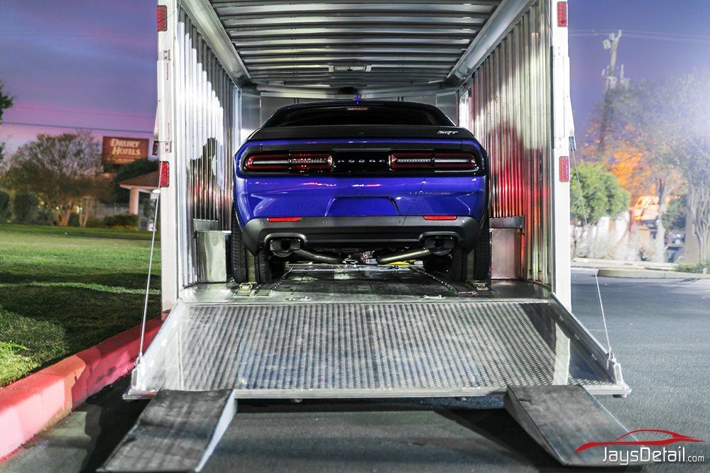 A blue Dodge Challenger being unloaded from a car hauler at dusk.